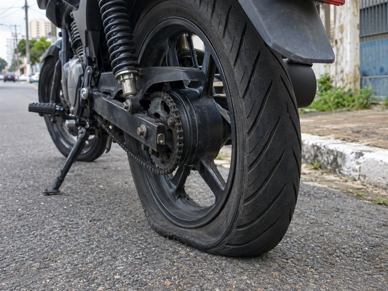 Pneu traseiro de moto furado encostado no asfalto